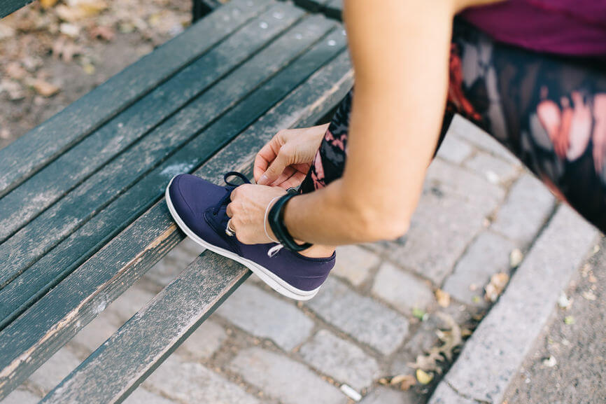 woman tying sneaker on green old bench